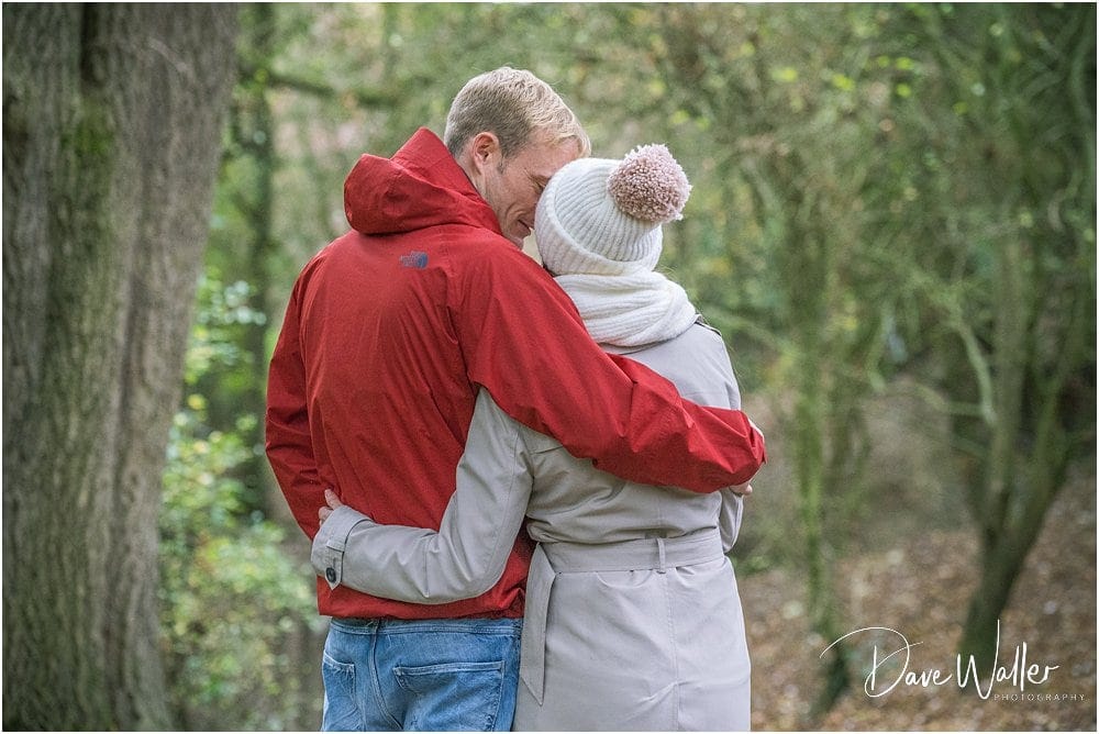 A couple in warm clothing embracing during their Autumn Engagement Shoot in a wooded area.