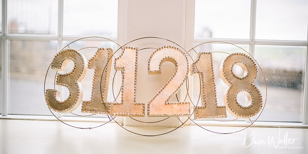 Golden sparkly numerals "3, 1, 2, 1, 8" arranged neatly on a windowsill, bathed in soft, natural light at a Halifax winter wedding.