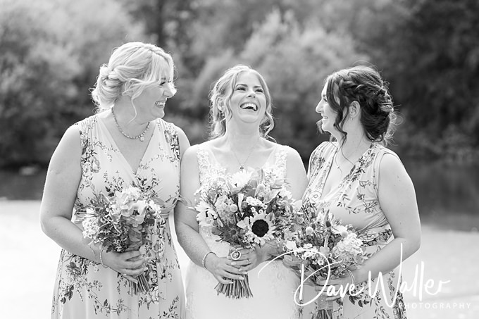 Bride and bridesmaids laughing, holding bouquets, black and white.