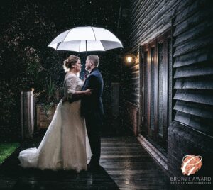 A romantic moment captured as a newlywed couple share an intimate gaze under an umbrella, while gentle rain adds a touch of magic to their nighttime embrace.