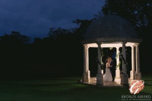 A romantic evening embrace under an illuminated gazebo, where a couple shares a tender moment in the serene twilight.