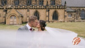 A newlywed couple sharing a romantic kiss with an elegant church in the background, commemorating their special day with a bronze award-winning photograph.