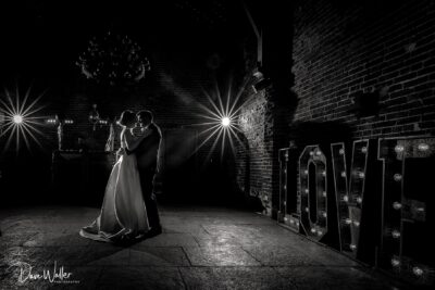 Newlyweds embraced in a romantic dance, illuminated by the sparkling glow of love, under the intimate ambiance of a dimly lit venue.