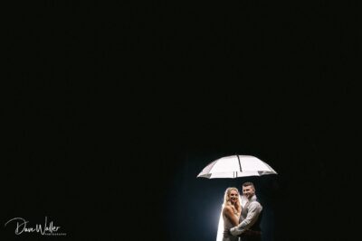 A couple sharing a tender moment under an umbrella, illuminated in a spotlight of love against a dark backdrop.