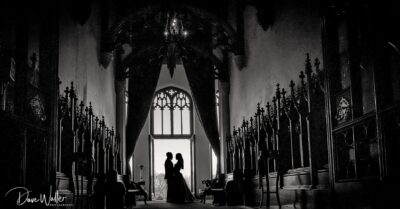 Silhouetted embrace: a couple shares a tender moment in the tranquil ambiance of a gothic church, framed by the grandeur of an arching window and the hushed reverence of shadowed pews.