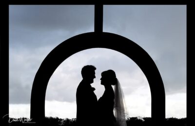 A silhouetted couple sharing a tender moment under an archway, set against a dramatic sky.