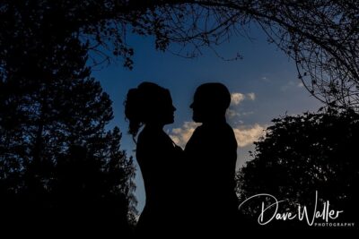 Silhouetted embrace: a couple shares a tender moment under a twilight sky, framed by the serene outline of nature, captured by an expert Leeds Wedding Photography.