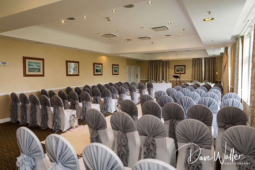 An elegantly set event hall at Hollins Hall Hotel with rows of chairs covered in white and gray fabric, ready for the wedding of Sophie & Nicholas.