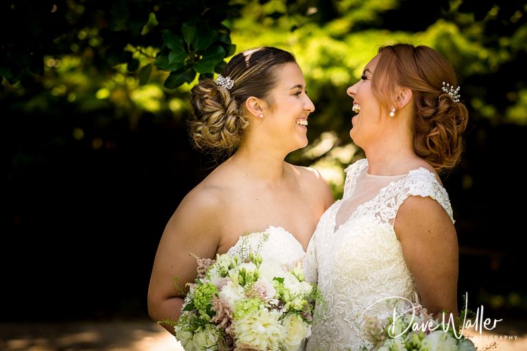 Two brides, Ella & Sophie, sharing a joyous moment on their wedding day, surrounded by natural beauty.