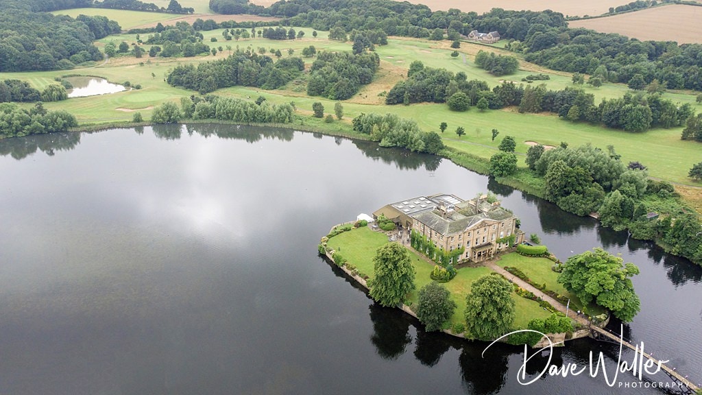 A serene aerial view of an elegant estate by the lakeside, captured by Sanchia, the Waterton Park Wedding Photographer, surrounded by lush greenery and tranquil waters.