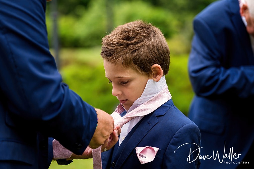 A young boy being gently adjusted in his smart blue suit by an adult out of frame, preparing for a formal occasion at Waterton Park.