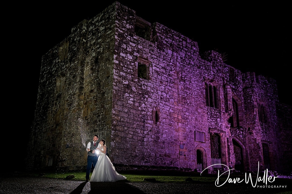 A magical evening: newlyweds share an intimate moment under the radiant glow of a majestic, illuminated Barden Tower Wedding castle wall.