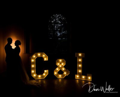 A romantic silhouette of a couple against a warmly lit "c&l" marquee sign, capturing an intimate moment likely celebrating their union.