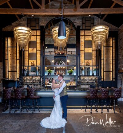 An elegant couple sharing a romantic moment on the dance floor, enveloped by the warm ambiance of a chic bar with exposed brick walls and stylish pendant lighting.