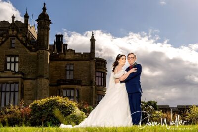 A happy couple sharing an embrace under a bright sky, with a majestic old building in the background, celebrating their wedding day.