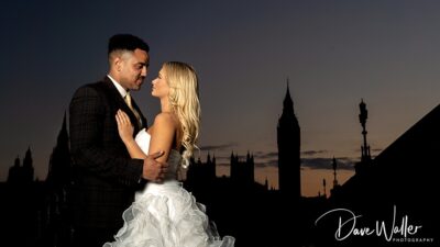 A couple in wedding attire shares an intimate moment against a captivating backdrop of an evening sky, with silhouettes of iconic architecture in the distance.