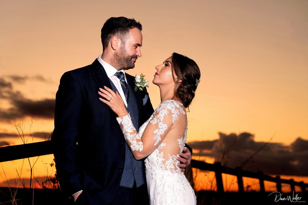 A newlywed couple, Emily & Duncan, sharing an intimate moment at sunset after their Wentbridge House Wedding, with the radiant sky providing a stunning backdrop to their embrace.