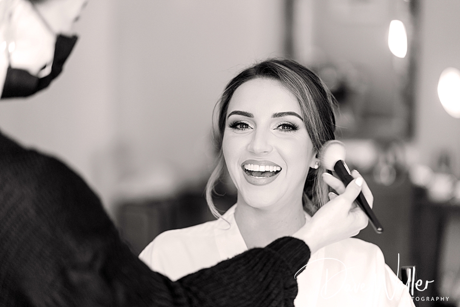 A radiant woman smiles joyfully at her Wentbridge House Wedding as she gets her makeup done, capturing a moment of beauty and preparation for Emily & Duncan's big day.