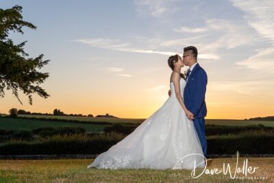 A couple in wedding attire sharing an intimate moment in a serene field at sunset.