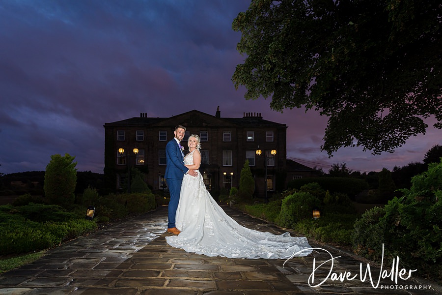 Newlyweds Hollie & Matt sharing a moment under a twilight sky in front of an elegant manor.