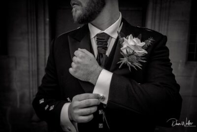 A groom in a black tuxedo adjusting his cufflinks with a boutonniere pinned to his lapel, moments before the ceremony.