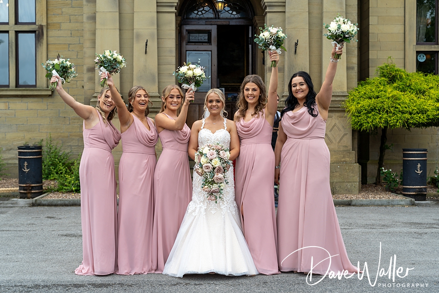 A joyful bride with her bridesmaids, all beaming and raising their bouquets, celebrating Lorna & Daniel's wedding day at Bagden Hall Hotel.