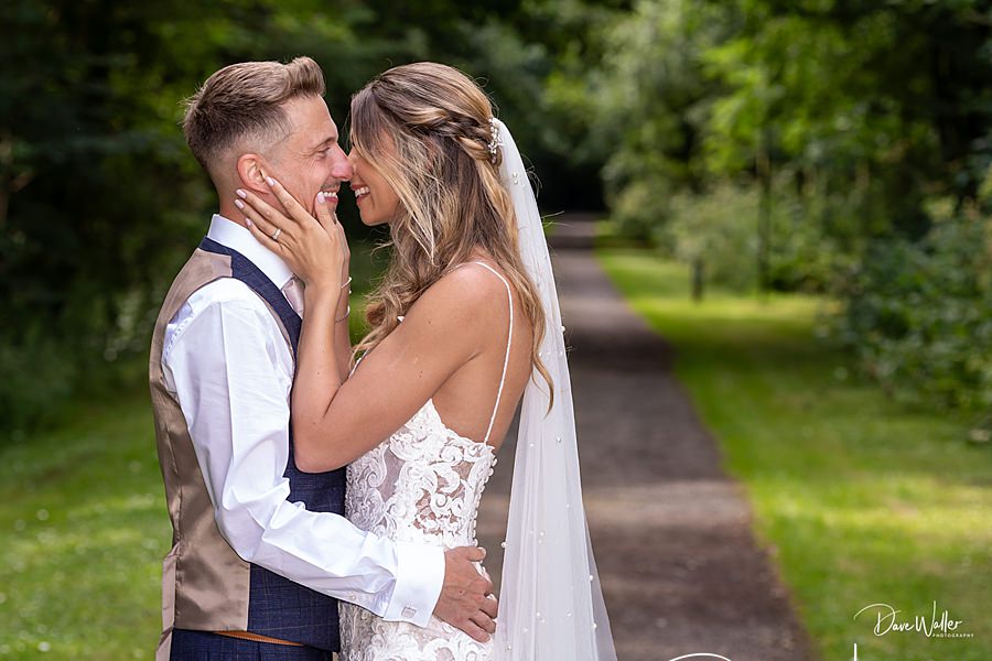 A joyful bride and groom sharing a tender moment outdoors at Sandburn Hall, with the bride gently touching the groom's face and both smiling lovingly at each other.