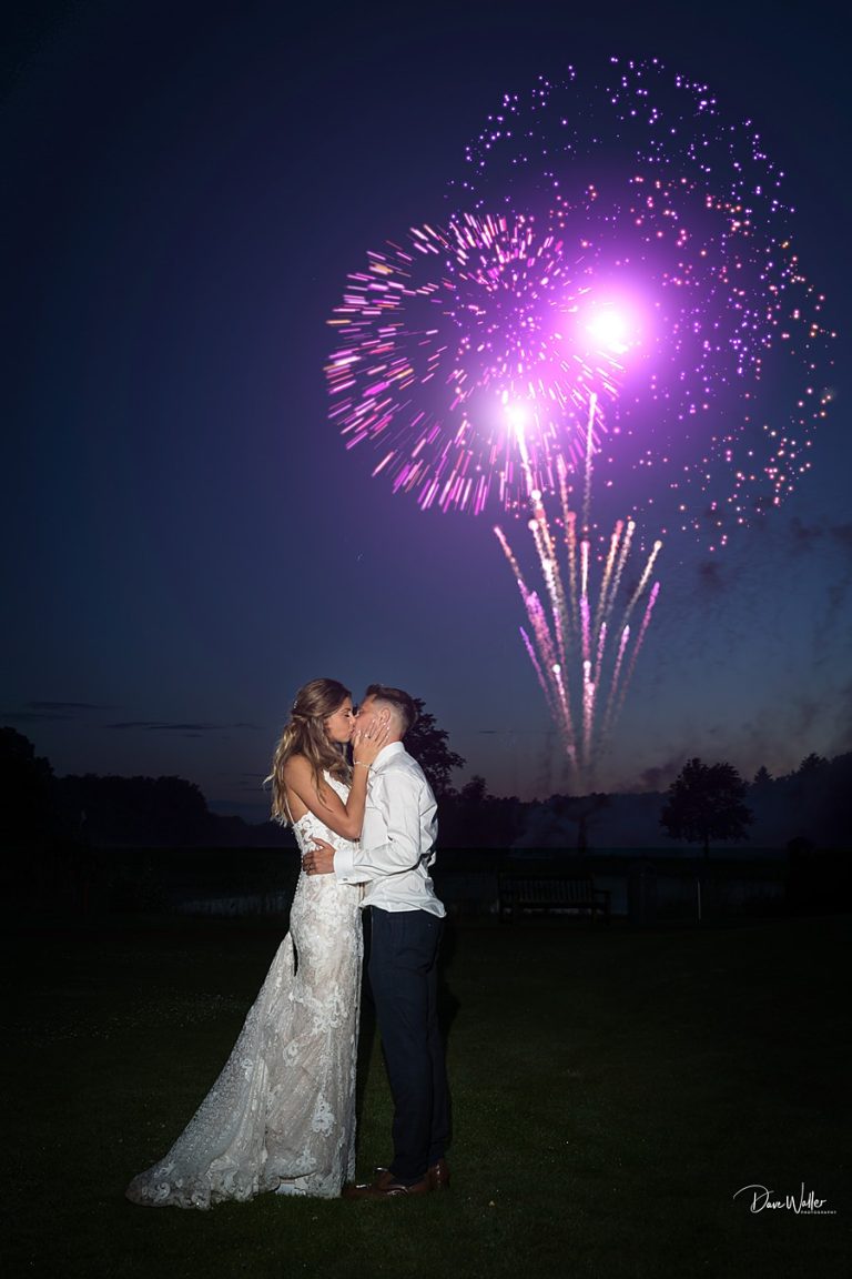Sally and Ryan share a romantic kiss under a dazzling display of fireworks at Sandburn Hall in a nighttime celebration.