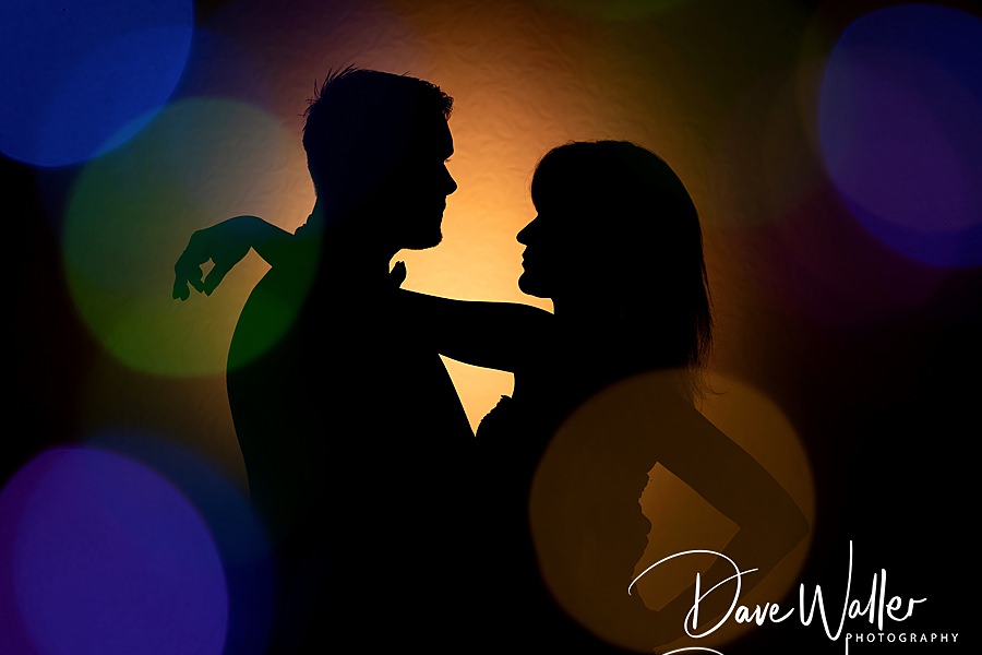 Silhouetted couple sharing a romantic moment at their Sandburn Hall wedding, surrounded by a colorful bokeh of lights.