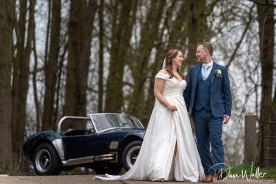Couple in wedding attire with vintage car background.