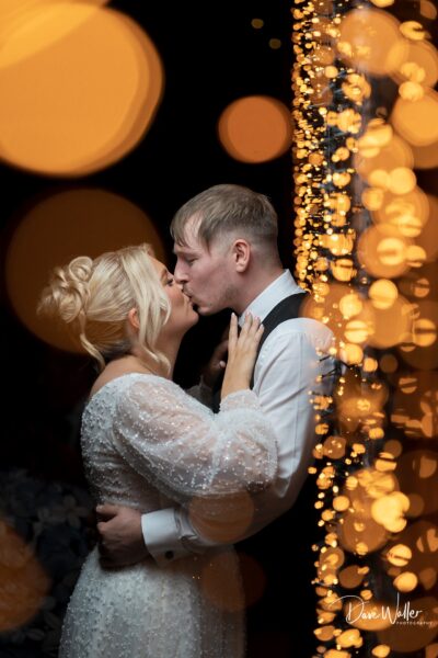 Couple kissing surrounded by festive lights.