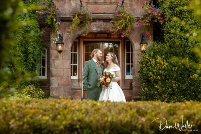 Bride and groom smiling outside building with flowers.