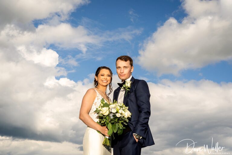 Couple posing on wedding day with cloudy sky.