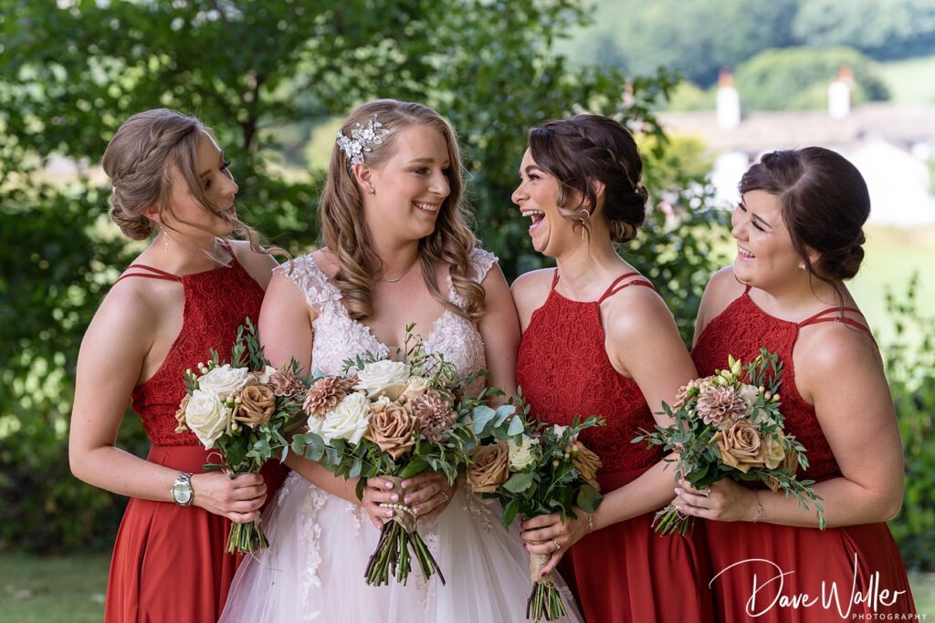 Bride and bridesmaids laughing with bouquets outdoors.