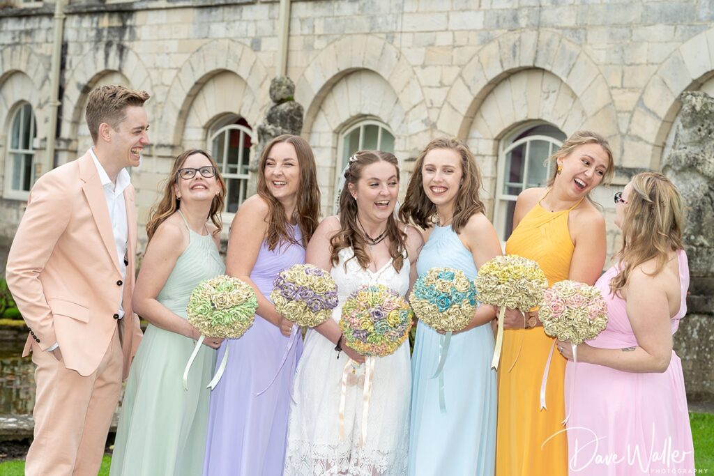 Wedding party laughing with colorful bouquets outdoors.