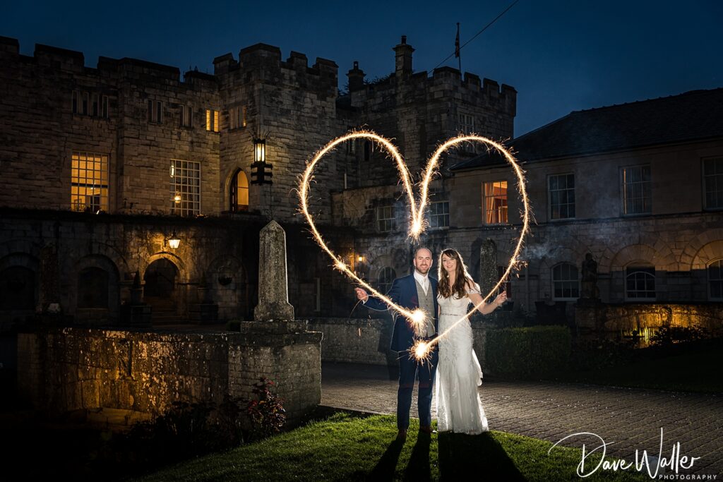 Couple with sparklers forming heart at night, castle backdrop.