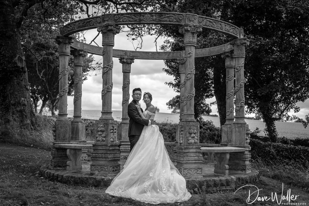 Couple embracing under ornate gazebo outdoors in monochrome.
