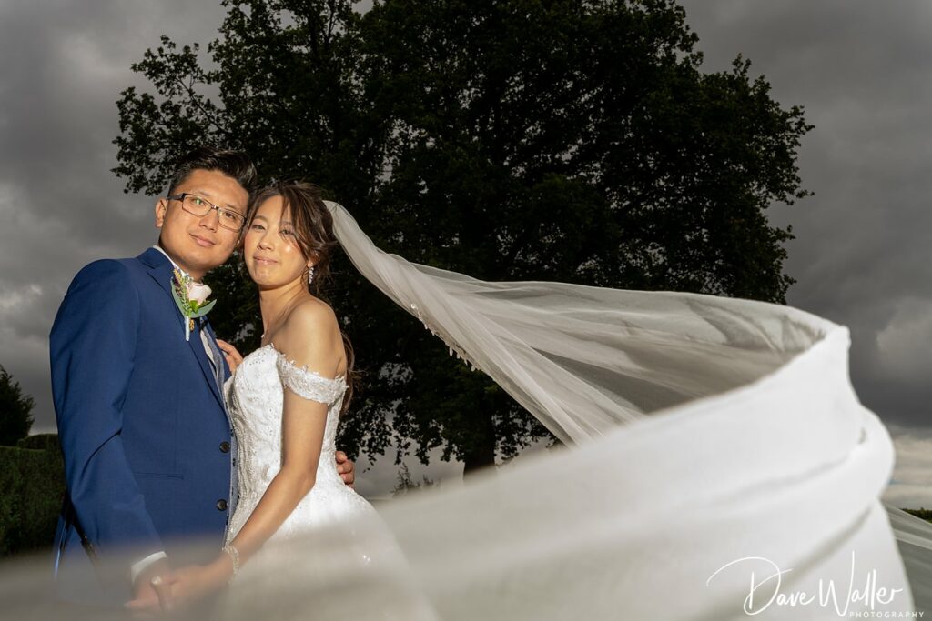 Couple posing on wedding day, veil fluttering.