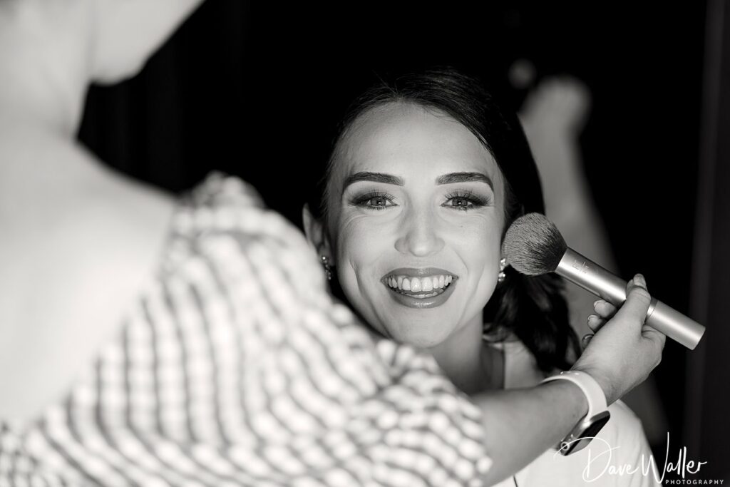 Woman smiling during makeup application in black and white.