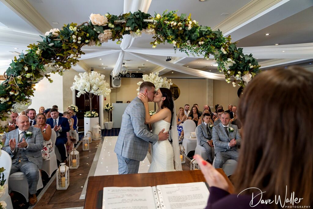 Couple kissing at wedding ceremony with guests.