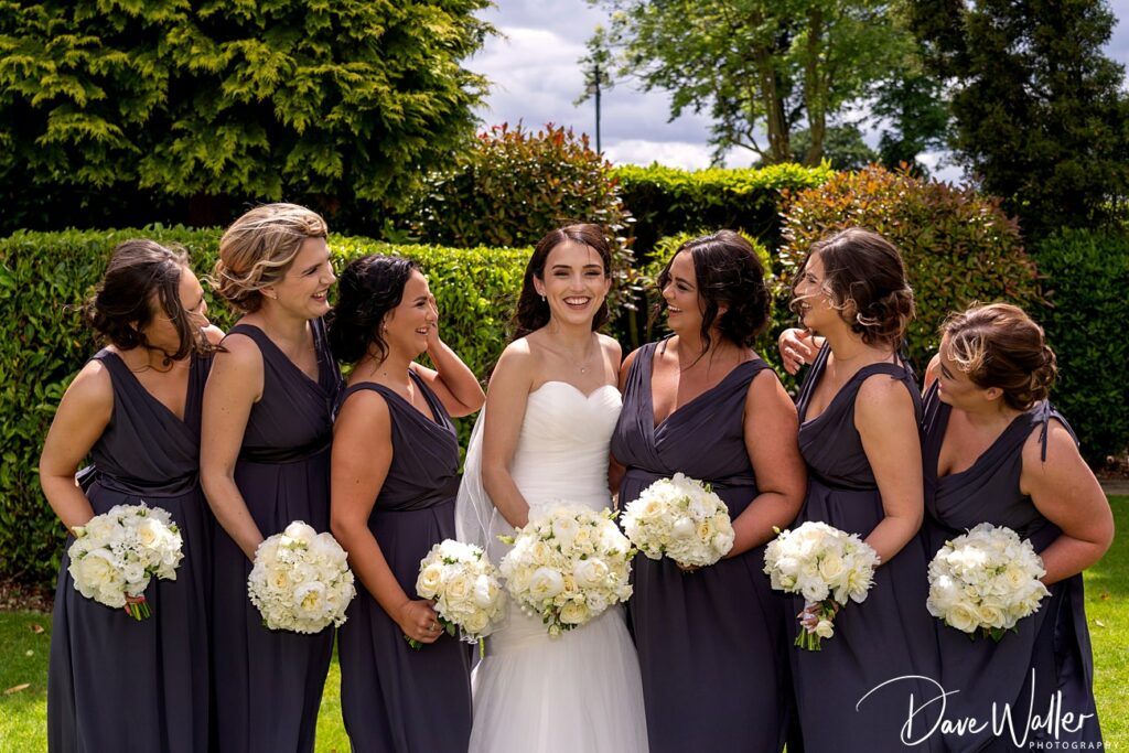 Bride and bridesmaids with bouquets, outdoor wedding smiles.