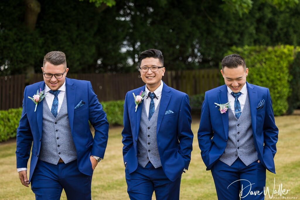 Three groomsmen smiling in blue suits at wedding.
