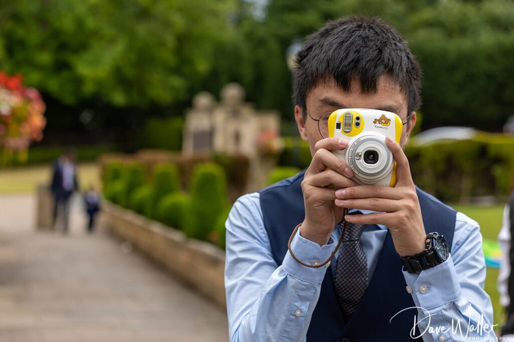 Man taking photo with yellow camera outdoors.