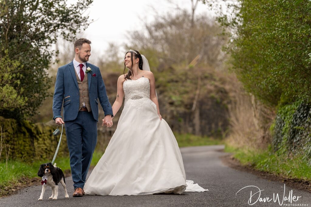 Wedding couple and dog walking on country road.