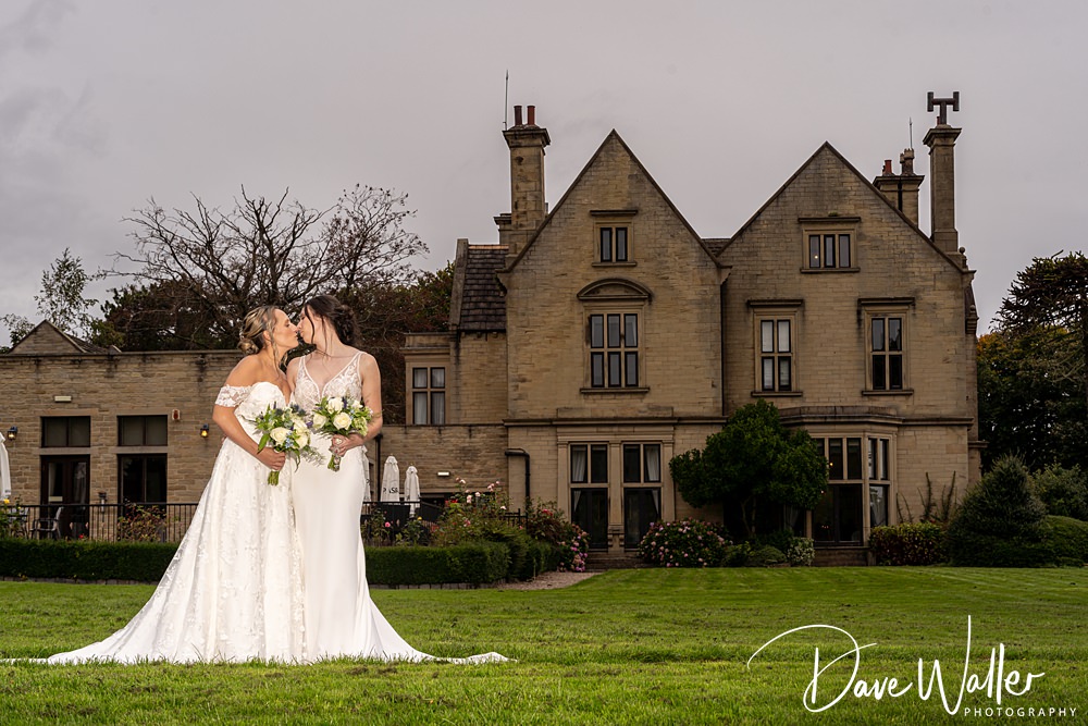 Bride couple kissing, historic manor backdrop, wedding day.
