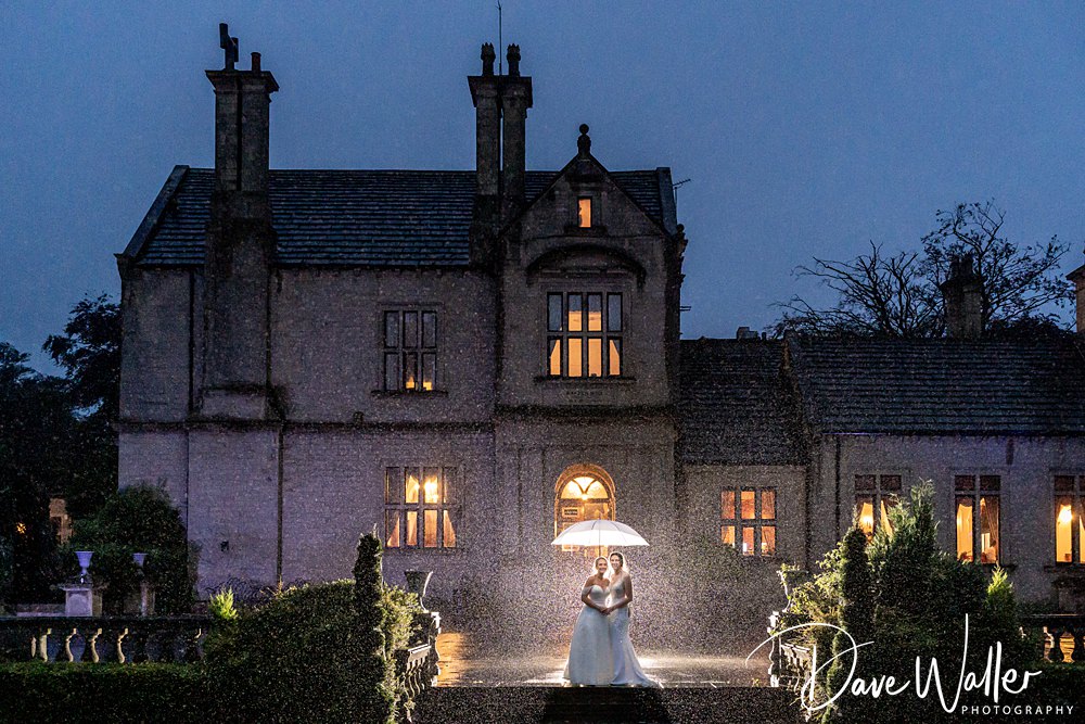 Bride and groom under umbrella at night, rainy manor wedding.