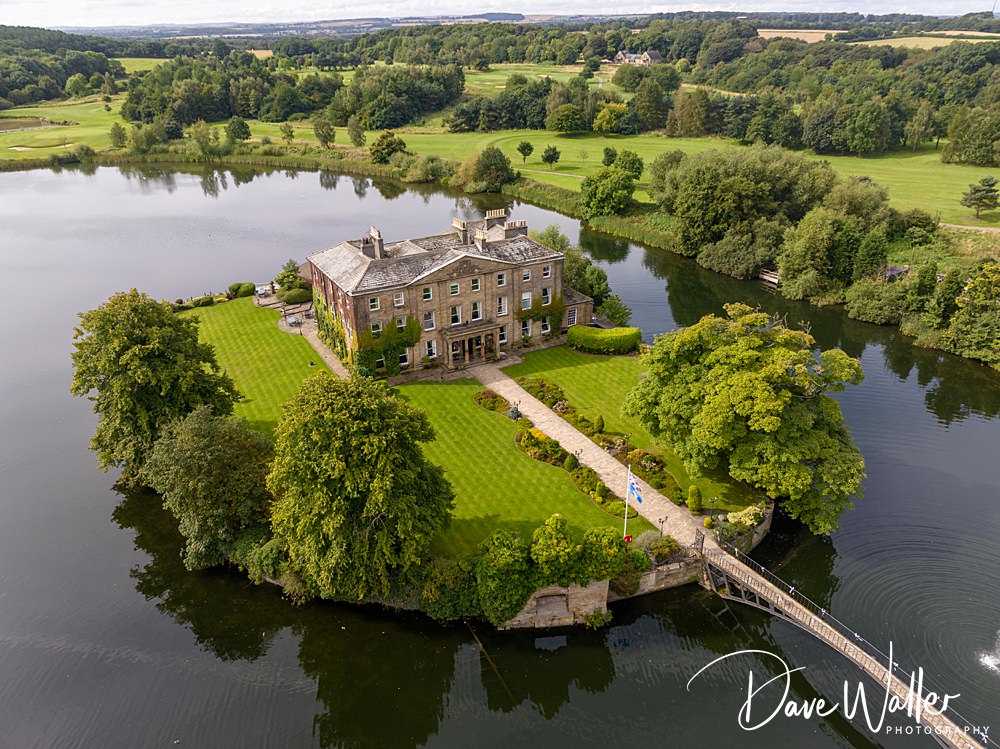 Aerial view of historic house on lush island with lake.