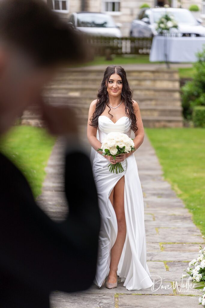 Bride walking down path with white roses bouquet.
