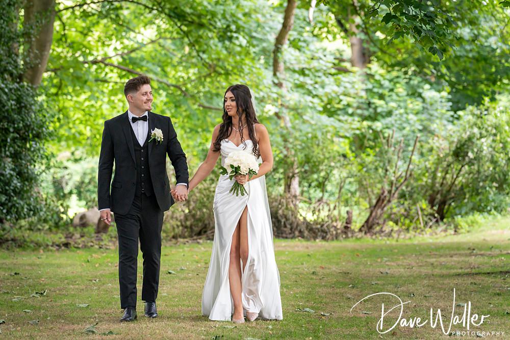 Couple walking in park, wedding attire, holding hands.