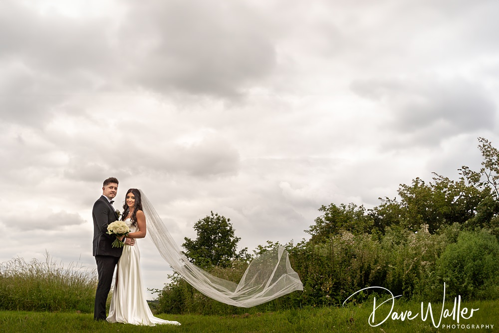 Bride and groom standing on a grassy field.